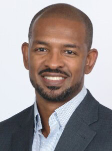 David McPherson, dressed in a suit jacket and collared shirt, smiles at the camera against a plain light background.