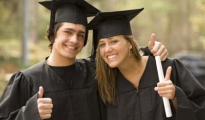 Two graduates in black caps and gowns smile and give thumbs up, celebrating their accomplishments. One person holds a diploma, a testament to the scholarship benefits that made this moment possible. Trees are visible in the background, adding to the joyous atmosphere.