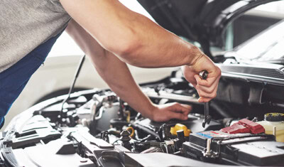 A mechanic uses a wrench to repair a car engine with the hood open, offering valuable vehicle maintenance tips to improve car mileage and fuel efficiency.