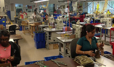 Workers at sewing machines in a factory with various materials and tools around them bustle with activity. At the Dallas Lighthouse for the Blind, this busy workspace thrives thanks to a generous Alliance Donation, enabling many to stay engaged in their tasks.