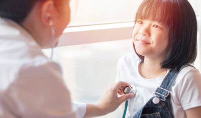 A healthcare professional uses a stethoscope to listen to a smiling child's heartbeat during a check-up, highlighting the importance of health care access for all.