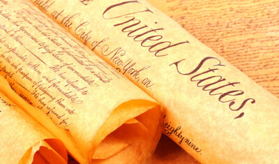 Close-up of a rolled parchment scroll with text beginning with "the United States" visible, referring to parts of a historical document, possibly an act Congress passed to repeal previous legislation.