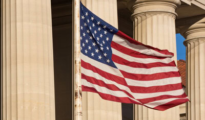 An American flag waves in front of a neoclassical building with large columns in the background, signifying the momentous occasion as the alliance commends the passage of the bill.