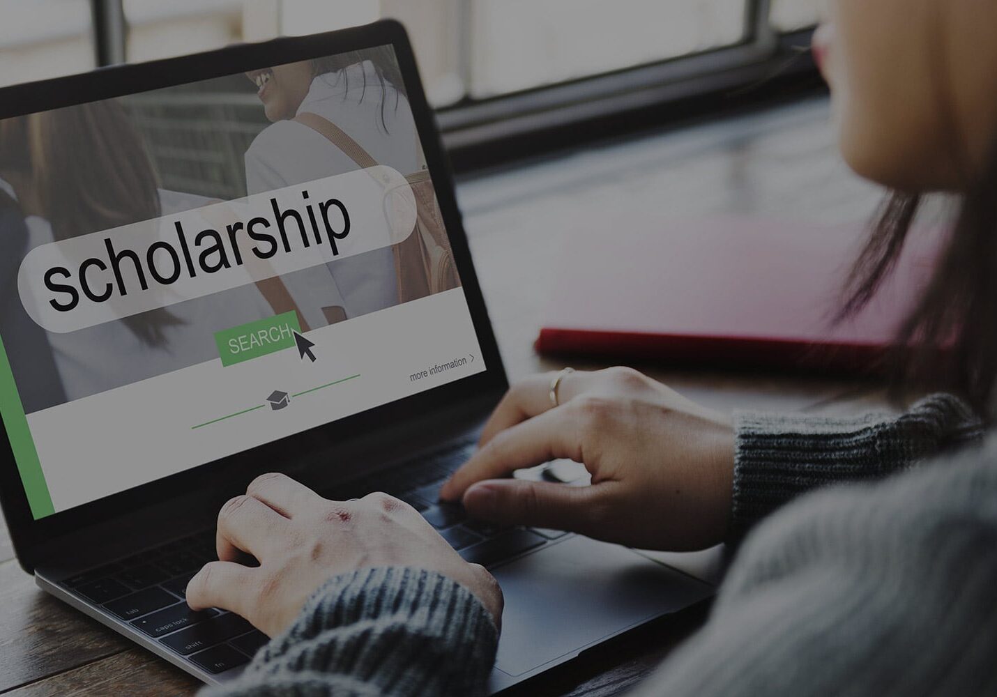 A person typing on a laptop with the screen displaying a search bar containing the phrase "college scholarships" and a search button.
