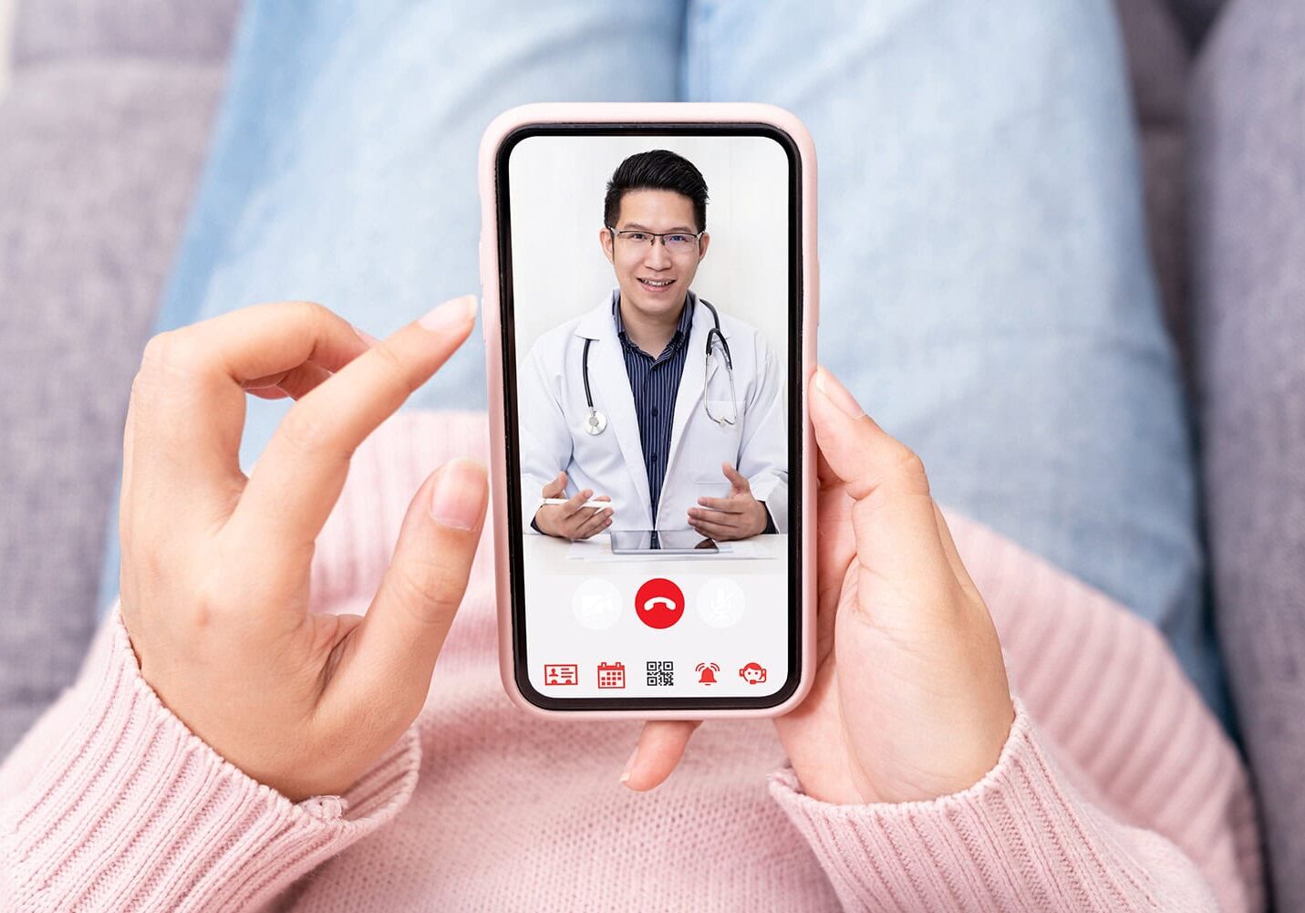 telemedicine-phone A person holds a smartphone displaying a video call with a doctor. The doctor, wearing a white coat and stethoscope, gestures with hands, emphasizing the direct benefits of this telehealth alliance.