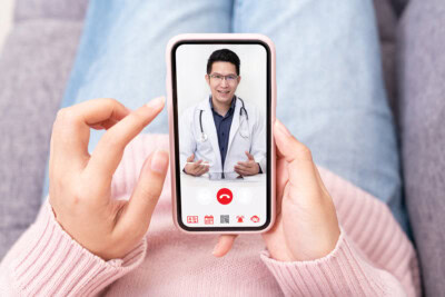 A person holding a smartphone displaying a doctor in a white coat and stethoscope during a video call, exemplifying the benefits of telehealth.