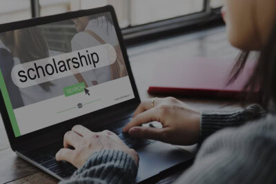 A person typing on a laptop with the screen displaying a search bar containing the phrase "college scholarships" and a search button.