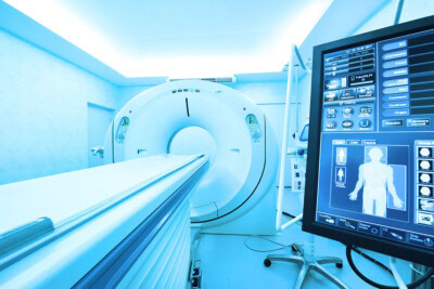 A CT scanner in a medical examination room with a control screen displaying diagnostic imaging options in the foreground.