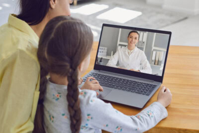 A woman and a child are having a video call with a doctor on a laptop, utilizing vacation health tips to ensure their trip remains worry-free.