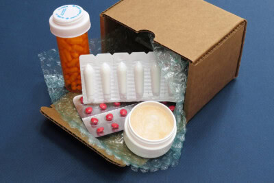 Cardboard box with bubble wrap containing a pill bottle, suppositories, blister pack of red pills, and a white jar with cream from MEDPro's Prescription Assistance program.