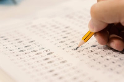 A hand holds a pencil, methodically filling in bubbles on a multiple-choice answer sheet, a familiar ritual for those preparing for standardized tests.