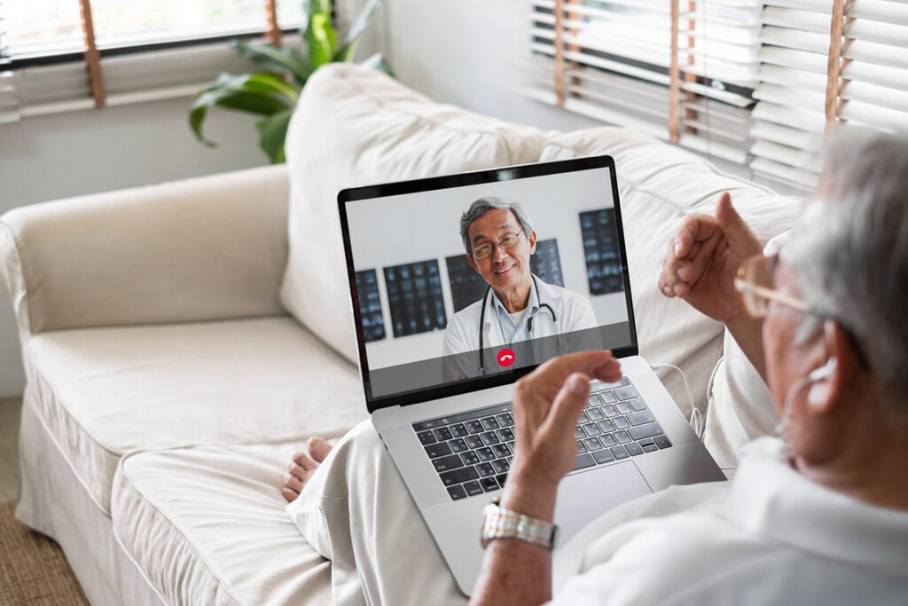 An elderly person is sitting on a couch, receiving a video call from their doctor on a laptop. The doctor serves as a helpful guide, ensuring the patient understands everything clearly.