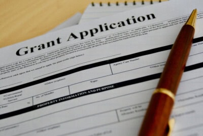 Close-up of a grant application form with a pen resting on it, placed on a table. The form has sections for personal information, funding type, and project details. A spiral notebook is seen in the background. If you're looking for tips on How to Get Them, this form is your gateway to securing grants.