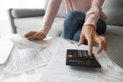 A student and parent use a calculator while surrounded by various financial documents and receipts on a table, focusing on key facts regarding student loans.